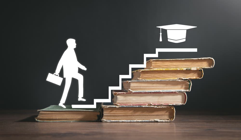 Silhouette of a person climbing a staircase of books toward a graduation cap